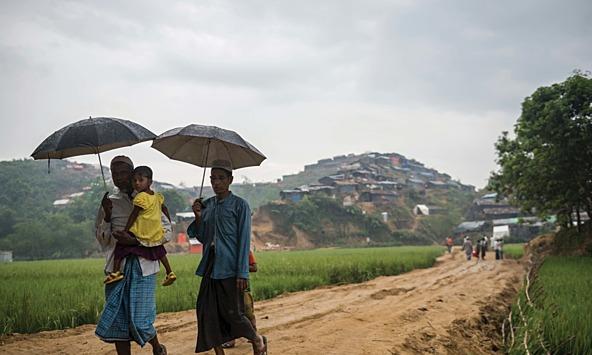 Rohingya Refugees walking with umbrellas holding a toddler